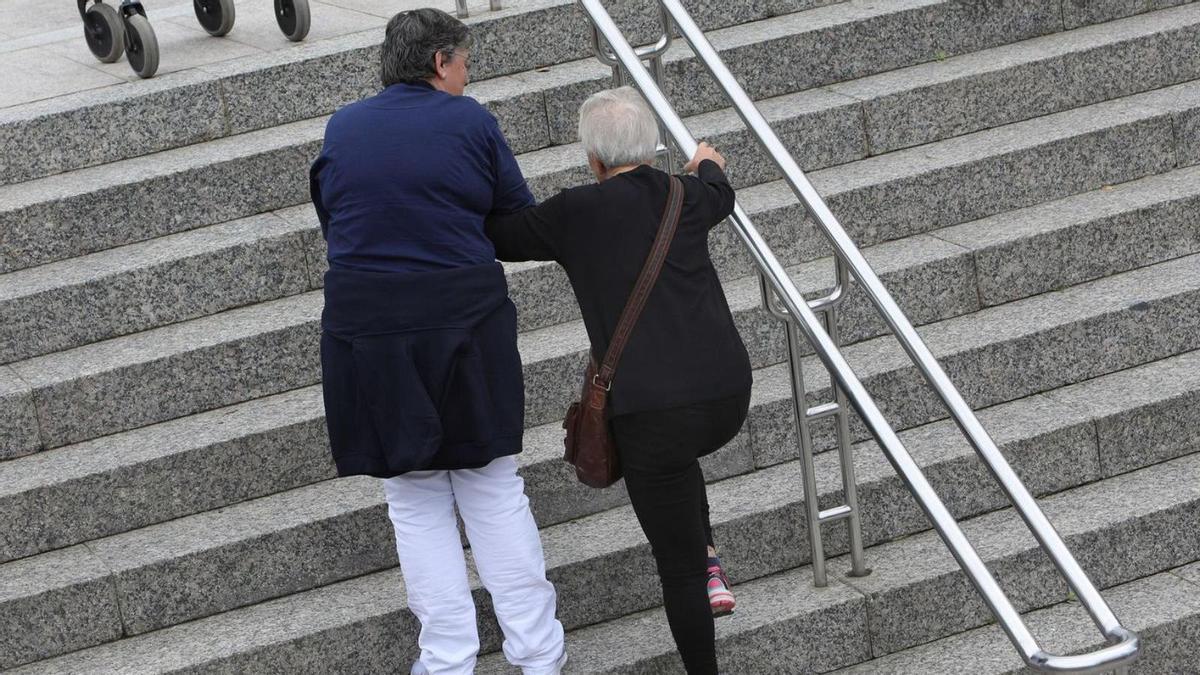 Una cuidadora ayuda a una mujer dependiente a subir unas escaleras en Santiago.