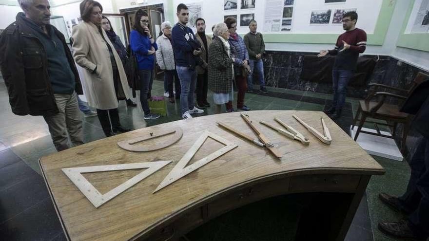 Asistentes a la inauguración de la exposición guiada por Rubén Domínguez, ante una mesa de profesor.