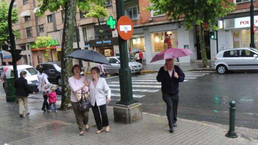 Viandantes por la calle Santa Rosa de Alcoy resguardándose de la lluvia con los paraguas.