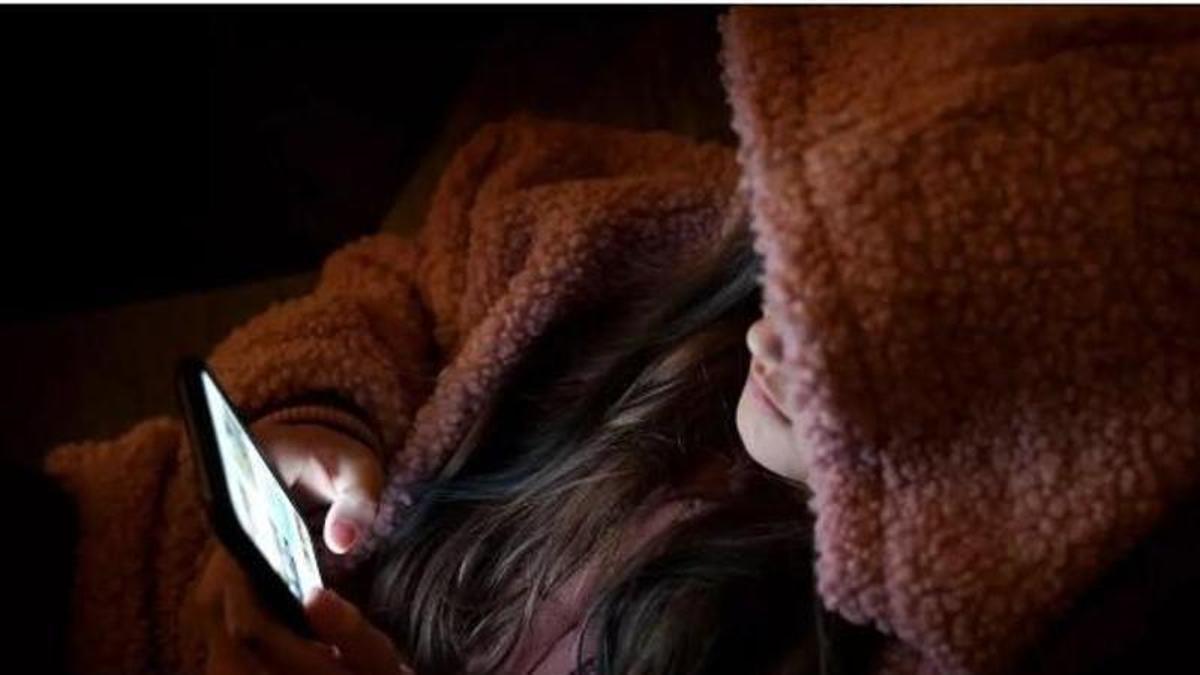 Una adolescent mirant el mòbil al sofá de casa seva