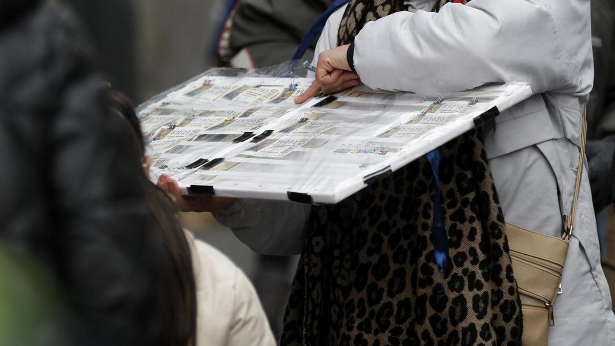 Una personas compra un décimo de lotería de Navidad a una vendedora ambulante