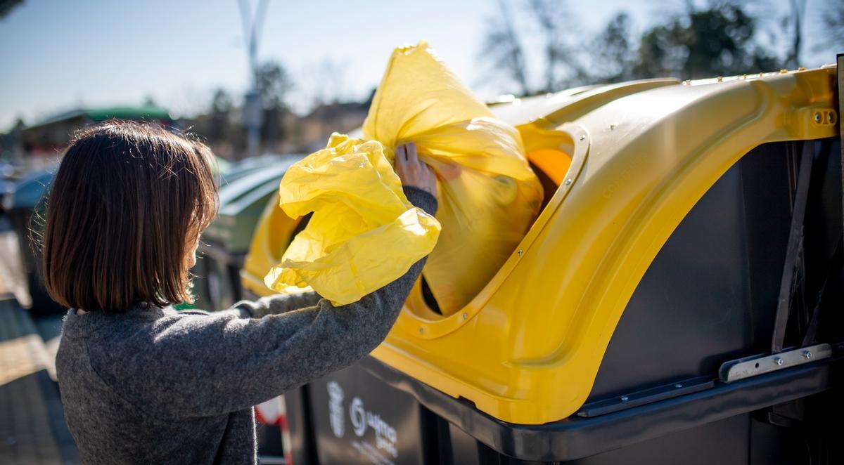 Una mujer tira una bolsa de basura al contenedor amarillo destinado al plástico.