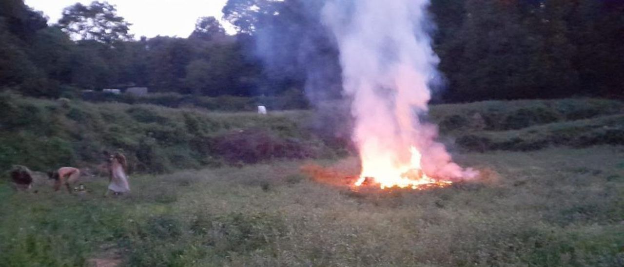 Imatge de la foguera i, a l'esquerra, tres de les persones que hi feien el ritual, anit