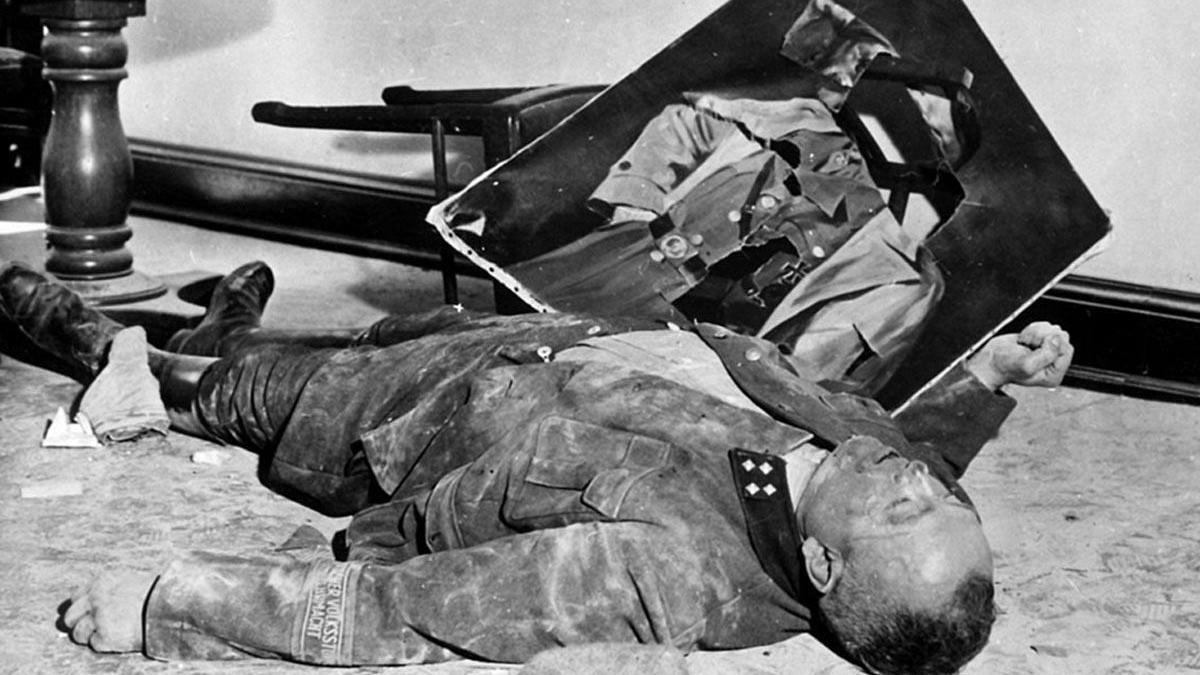 El comandante nazi del batallón de la Volkssturm, Walter Dönicke, tras envenenarse, junto a un retrato desgarrado de Adolf Hitler.