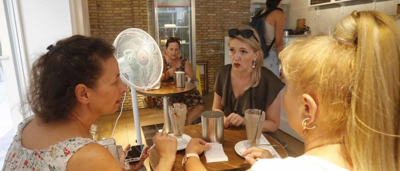 Tres mujeres meriendan en una heladería con un ventilador de fondo para enfríar el local. | JM LÓPEZ