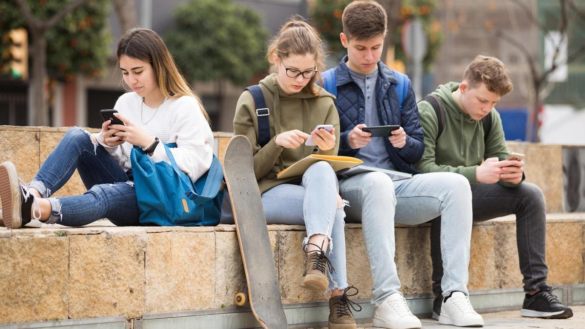 Varios jóvenes miran sus teléfonos móviles.