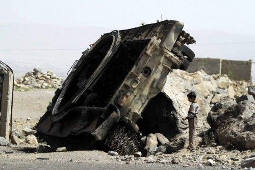 A boy stands near a destroyed armoured vehicle on a road in the northwestern province of Omran