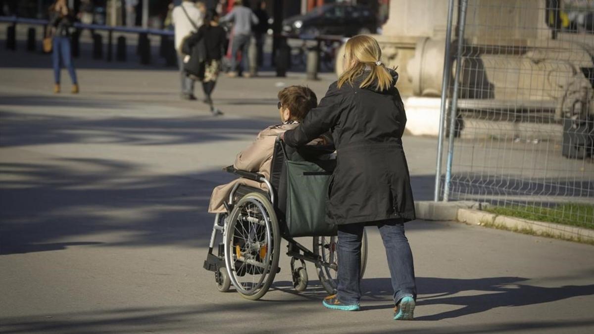 Una cuidadora acompaña a una mujer en silla de ruedas en Barcelona.