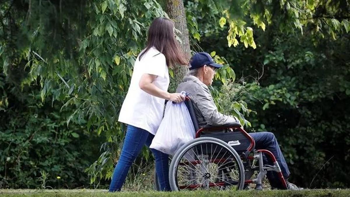 Una cuidadora ayuda a una persona con discapacidad en el paseo por un parque.