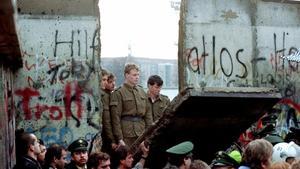 Guardias fronterizos de Alemania Oriental observan cómo la multitud de trae al piso un lado del muro. 