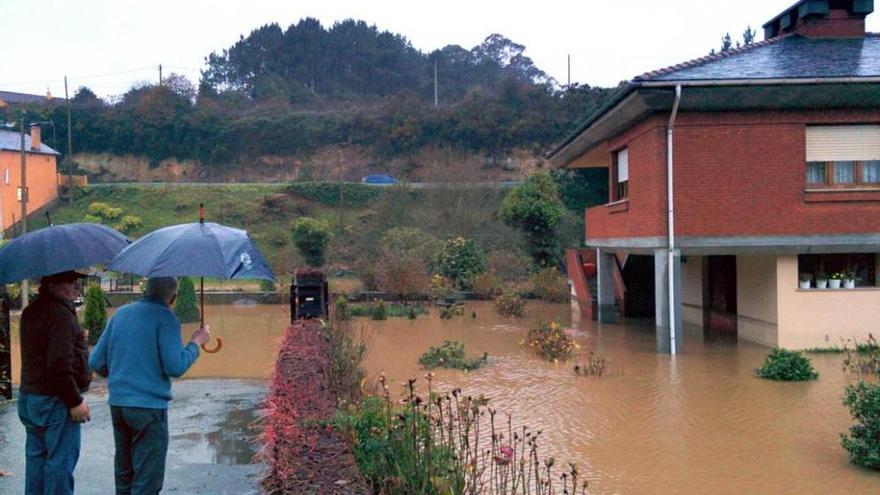 Dos vecinos contemplan el jardín inundado de una vivienda de El Viso, en Tapia de Casariego.