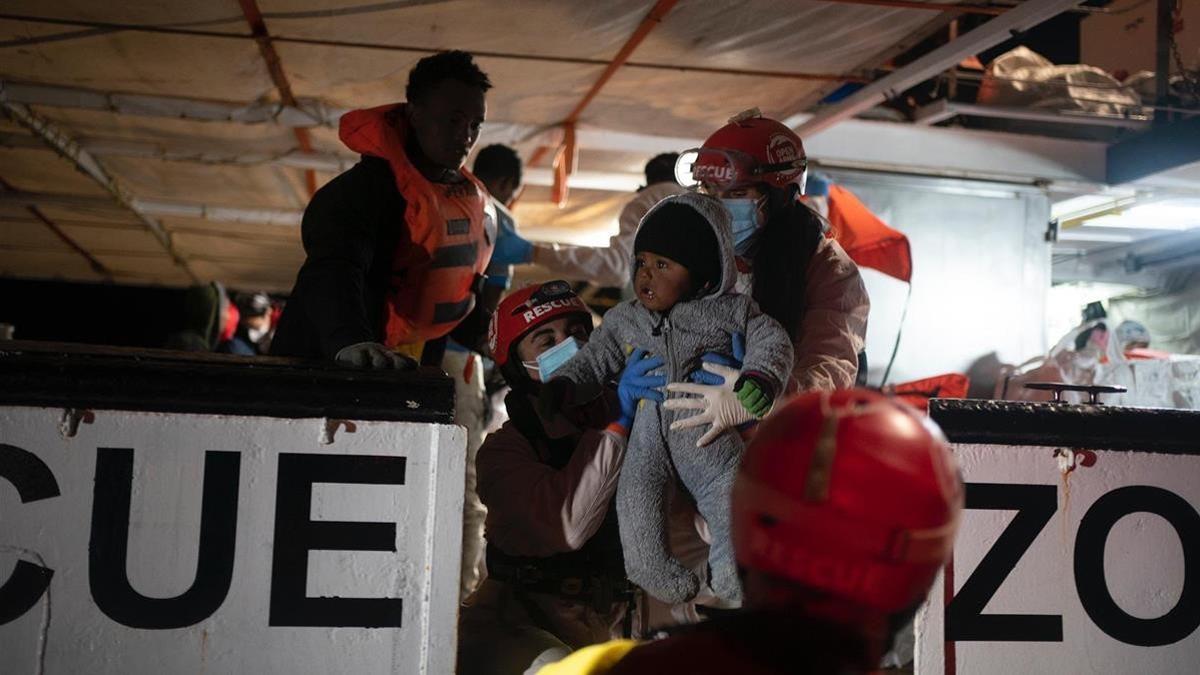 Miembros de la tripulación del 'Open Arms' ayudan a subir a bordo del barco a un bebé rescatado.