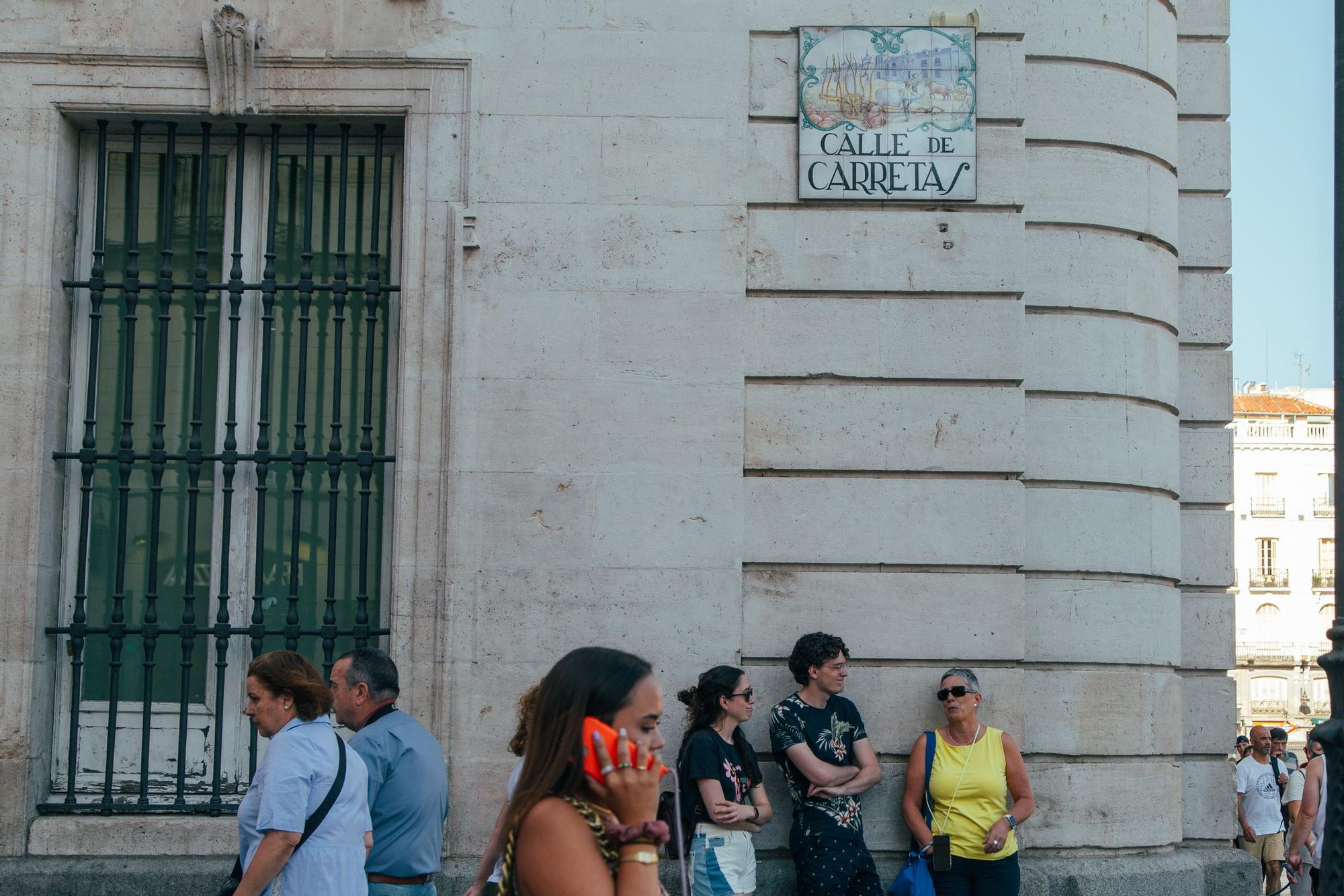 Varias personas transitan por la esquina de la calle de Carretas con la Puerta del Sol.