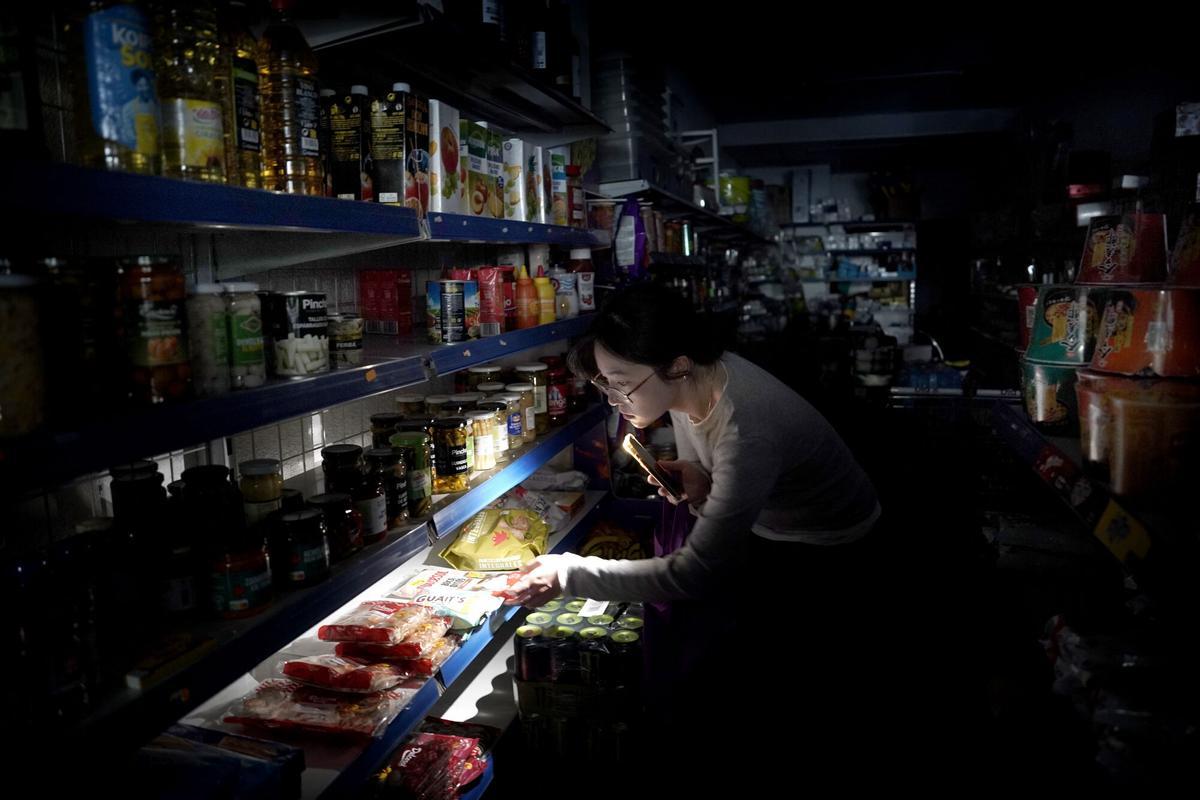Madrid. 28.04.2025. El mayor apagón eléctrico de la historia de España, ocurrido el lunes 28 de abril de 2025. Una mujer usa la linterna de su teléfono móvil para ver los estantes de una tienda. COMERCIO. NEGOCIO. ESTABLECIMIENTO. ESTANTERIAS. ELECTRICIDAD. CORTE DE ENERGIA ELECTRICA. LUZ. CORRIENTE. APAGON HISTORICO. CERO ENERGETICO