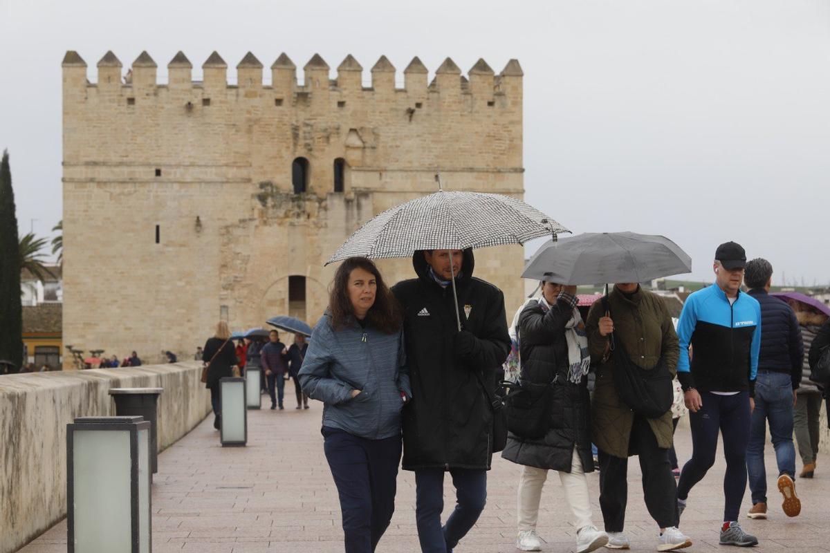 Varias personas caminan bajo la lluvia por el Puente Romano de Córdoba.