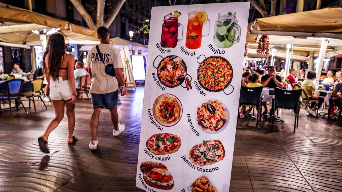 Un cartel anuncia bebidas alcohólicas y comida junto a las terrazas de la Rambla.