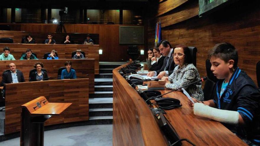 En primer término, el alumno Diego Suárez Díaz lee un poema desde la mesa de la Cámara, junto a Ana Cano y Pedro Sanjurjo.