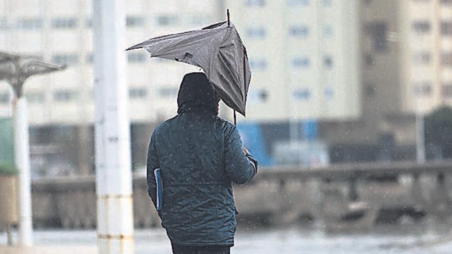 Un joven se protege de la lluvia con un paraguas roto en el paseo marítimo.