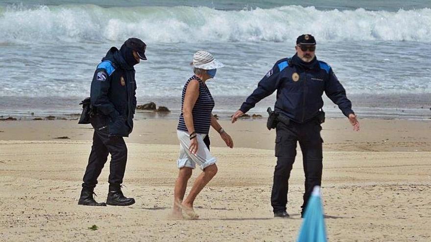 Dos policías locales de Sanxenxo con una mujer en la playa con mascarilla en el confinamiento.