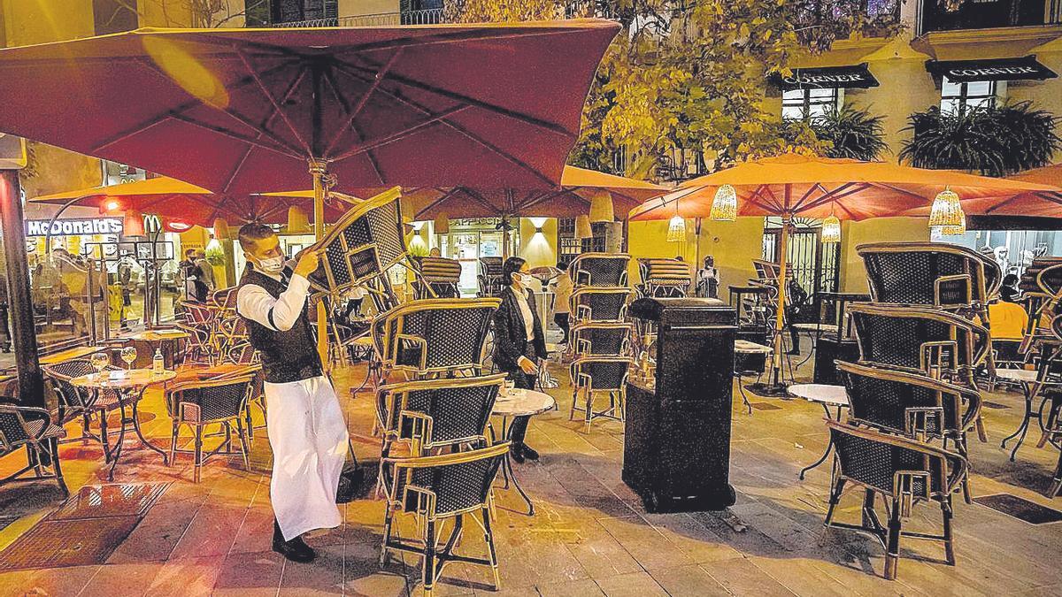 Un camarero de un establecimiento de la plaza Rei Joan Carles I recoge, ayer, la terraza.