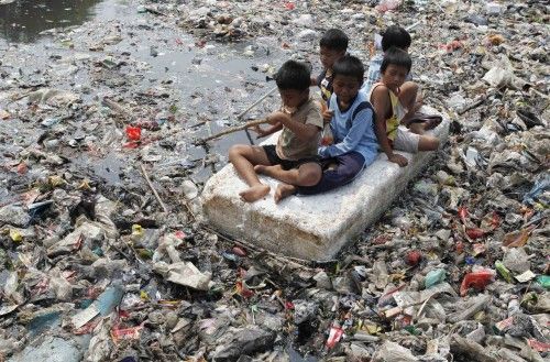 Children sitting on a makeshift raft play in a river full of rubbish in a slum area of Jakarta