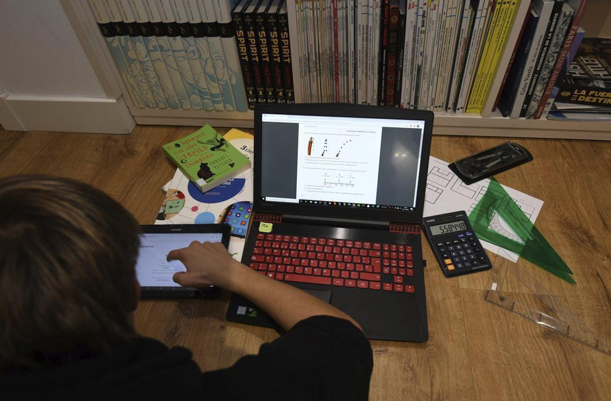 Un menor estudia con una táblet y un ordenador.