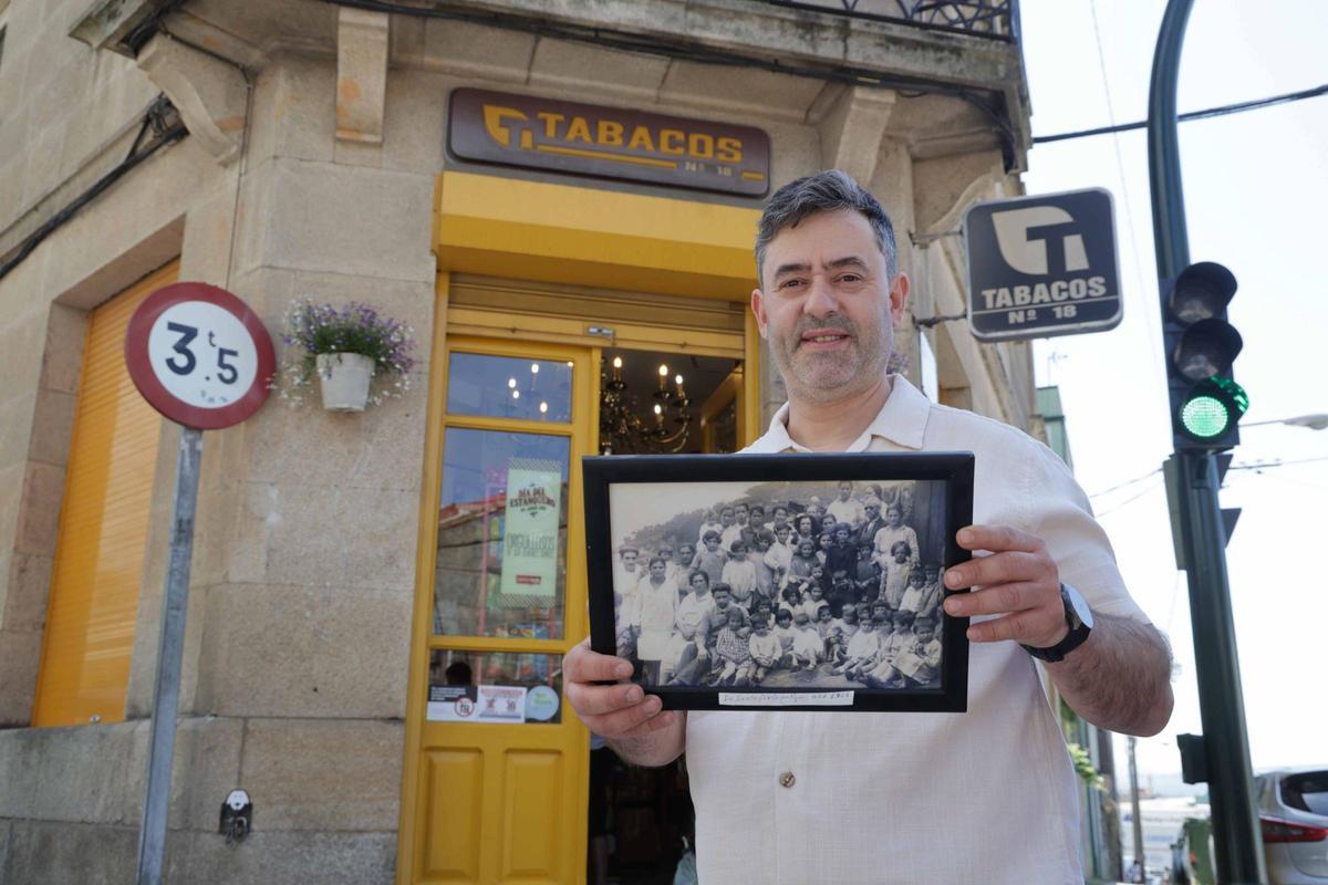 Moisés Rivera posa frente al estanco con una foto histórica, de 1925, en la que aparece su abuelo, el cuarto por la izquierda y hacia abajo.