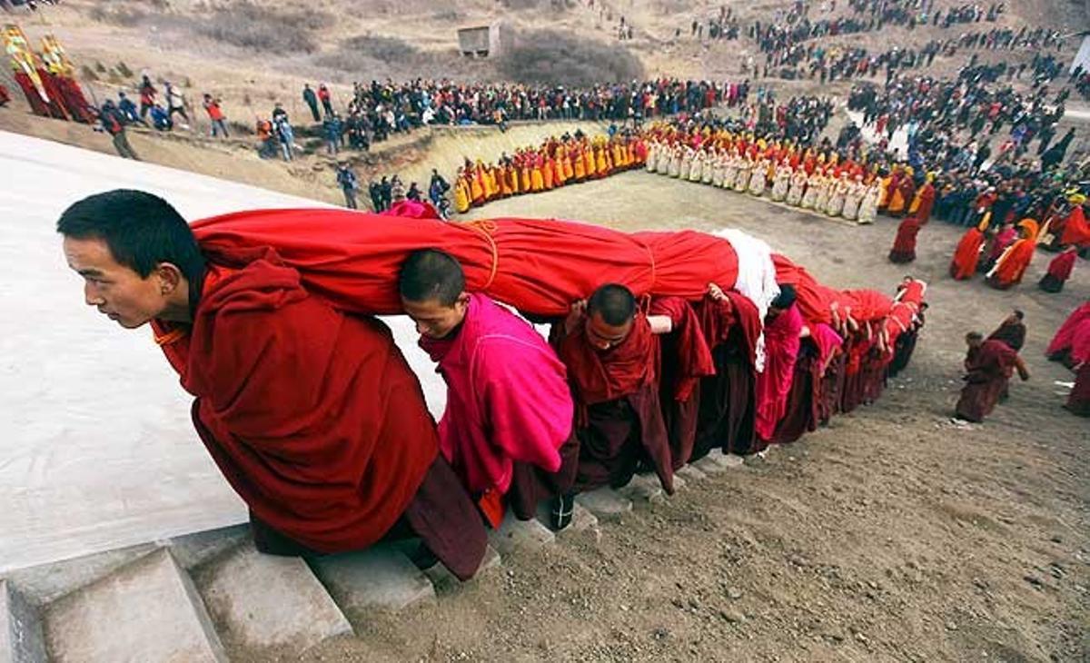 Budistes tibetans carreguen un ’thangka’ gegant, una pintura religiosa de seda amb brodats que durant el Gran Festival de l’Oració serà desplegada en un turó a prop del temple de Langmu a la Prefectura Autònoma Tibetana de Gannan, província de Gansu, Xina.