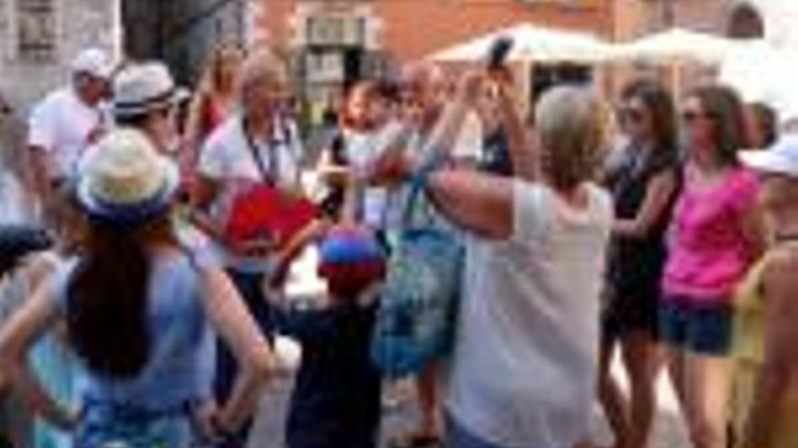 Un grup de turistes amb la seva guia, que porta penjat al coll un micròfon, i turistes caminant pel carrer de la Força de Girona.