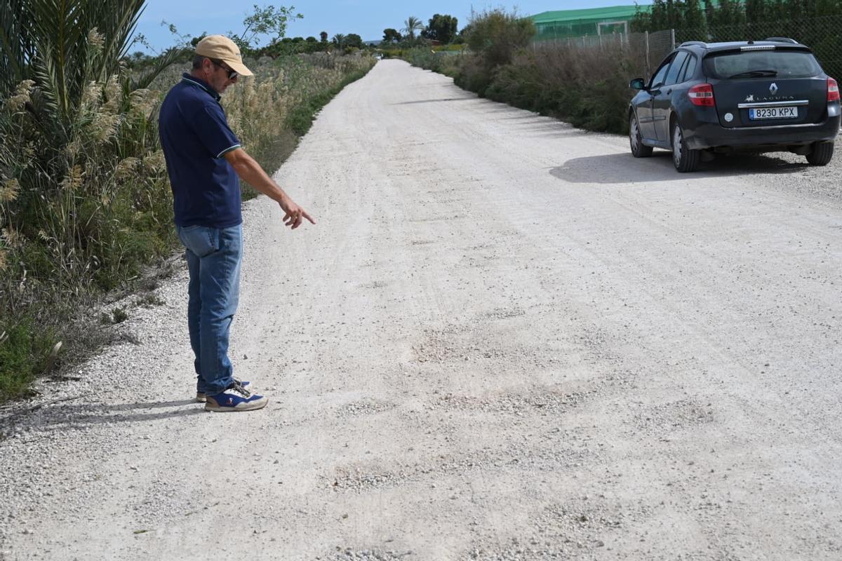 Un vecino señala los baches mientras pasan coches alrededor