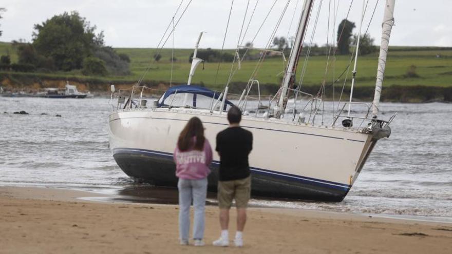 Dos personas contemplan desde la arena el velero varado en Bañugues. | R. Solís