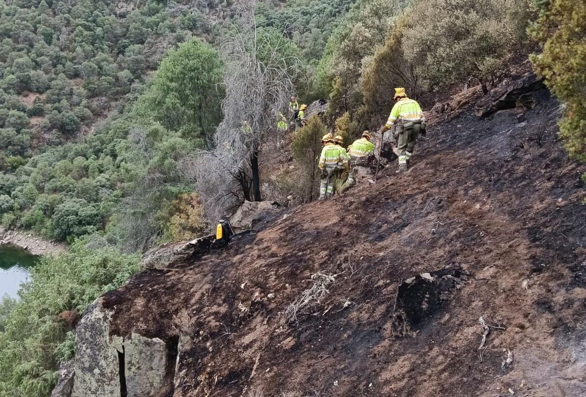 Bomberos forestales refrescan terrenos calcinados por el fuego.