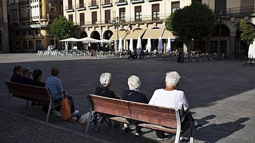 Mayores sentados en los bancos distribuidos en la Plaza Mayor de Zamora.