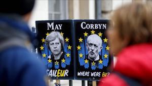 Unos peatones pasan junto a carteles con la primera ministra británica, Theresa May, y el líder del Partido Laborista, Jeremy Corbyn, cerca del Parlamento, en Londres.