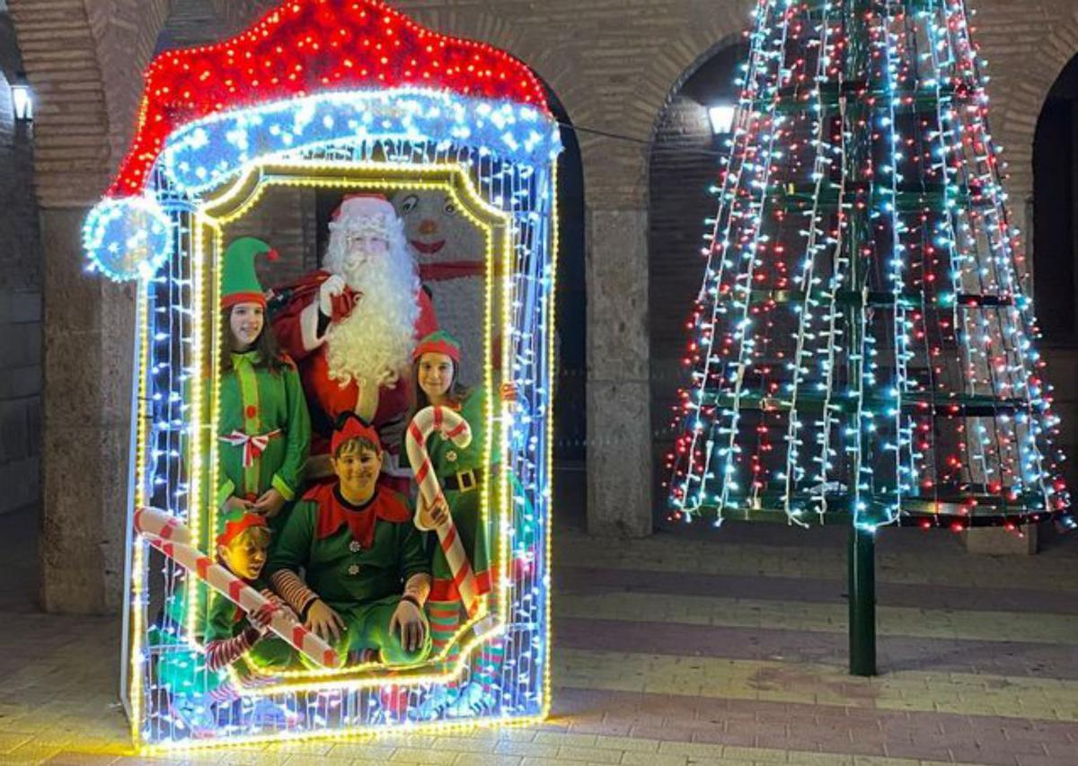 Papá Noel con los elfos junto al árbol.