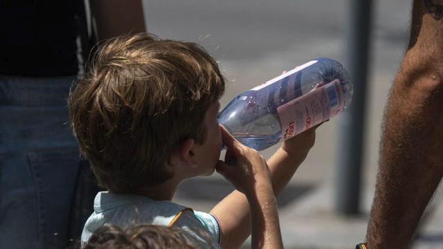 Un infant beu aigua al costat del seu germà petit, a Barcelona. | BELÉN GONZÁLEZ