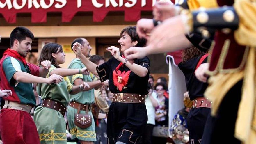 Cristianos de diferentes filaes, durante la ejecución de una de las danzas que componen el tradicional &quot;Ball Cristià&quot;. A la derecha, la plaza de España repleta de festeros durante la embajada