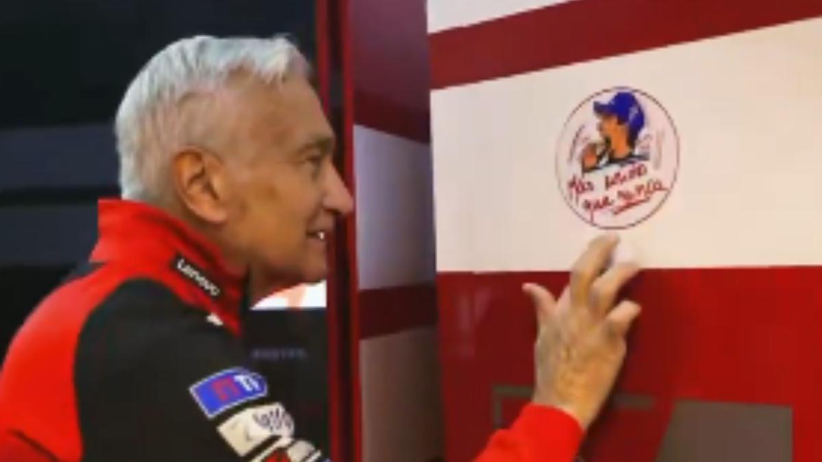 Davide Tardozzi pega una pegatina motivacional para Márquez en el box de Ducati