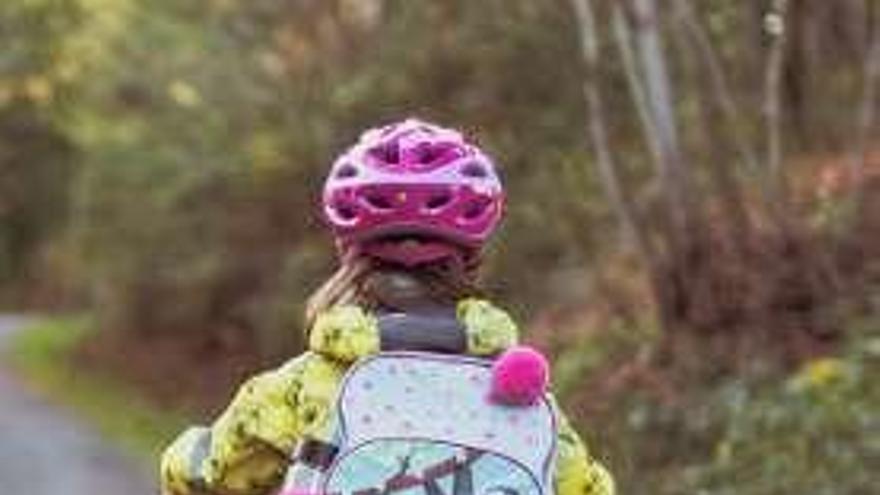 Una niña en bicicleta con su mochila escolar.