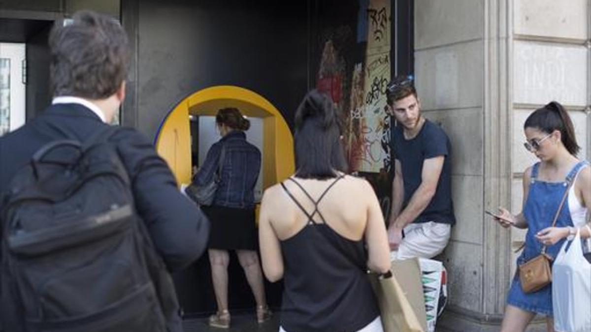 Varias personas esperan para operar en un cajero de una oficina de CaixaBank en la plaza de Catalunya