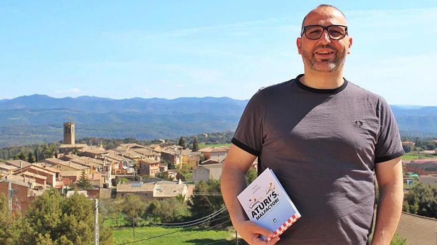 L&#039;agent Pep Fuster amb el llibre a les mans i el seu poble, Sant Feliu Sasserra, de fons