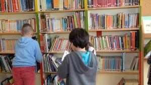 Tres alumnos de primaria consultan libros en una biblioteca escolar.