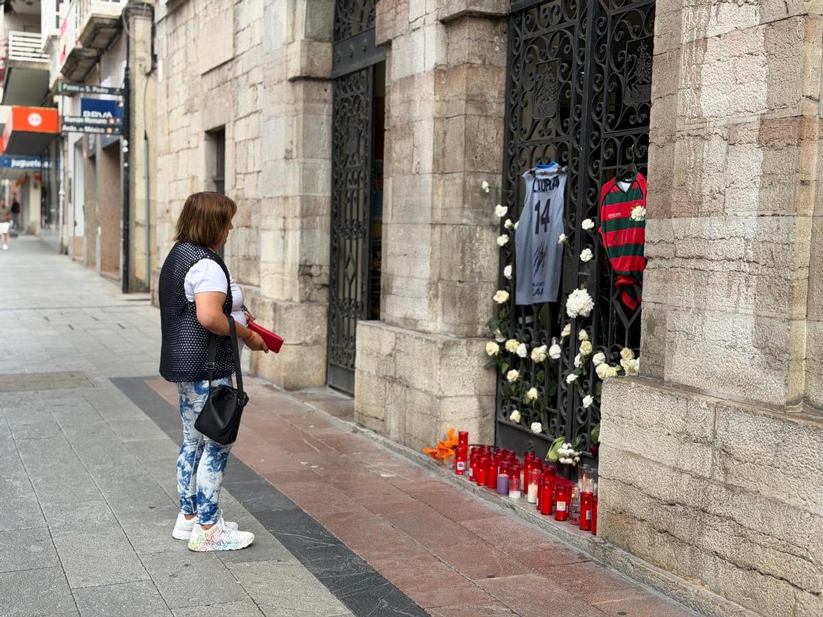 Una mujer en Llanes, frente a la portilla en la que se homenajea a Laura Cruz con las camisetas de los equipos locales de baloncesto y rugby