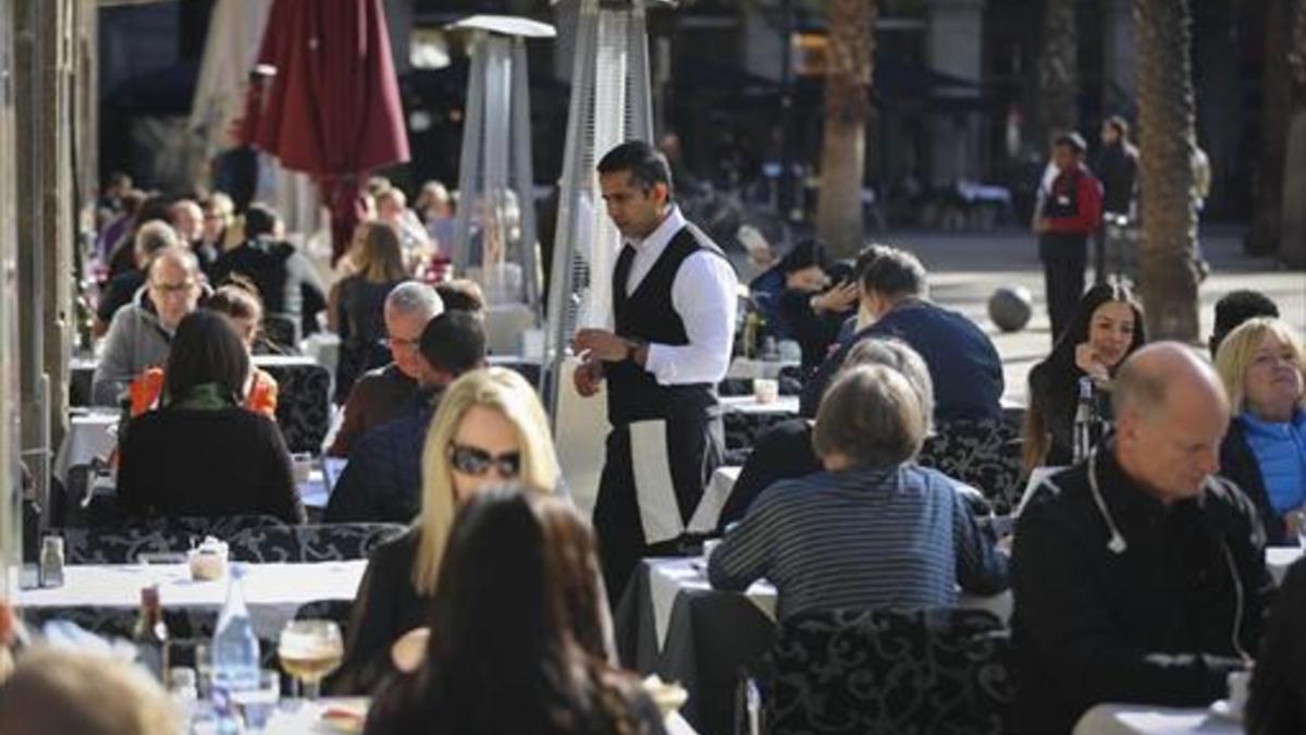 Un camarero atiende a los clientes de una terraza de la plaza Reial de Barcelona.