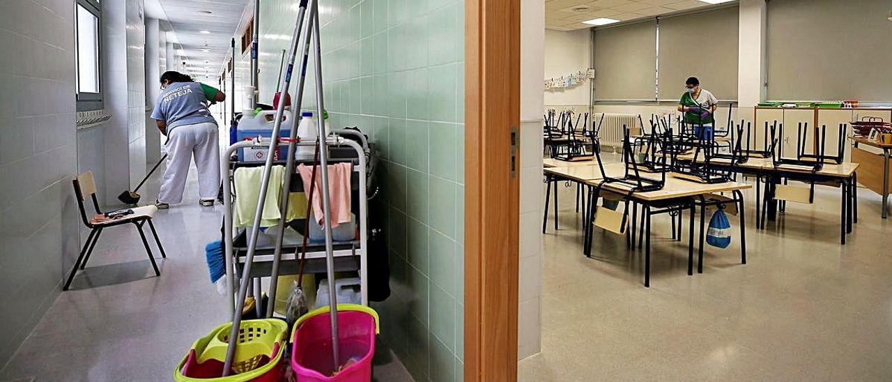 Dos trabajadoras del servicio de limpieza desinfectan los pasillos, sillas y pupitres de una clase de infantil de un colegio.