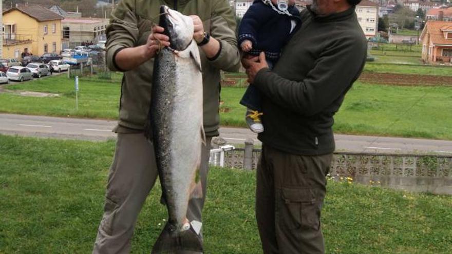 Israel Curiel Martínez posa con el salmón de 10,2 kilos y 95 centímetros de largo que pescó el pasado viernes en el Narcea. A su lado, su padre, Mariano Curiel Garrido, sostiene en brazos a Pacho Curiel Noval, hijo del pescador.