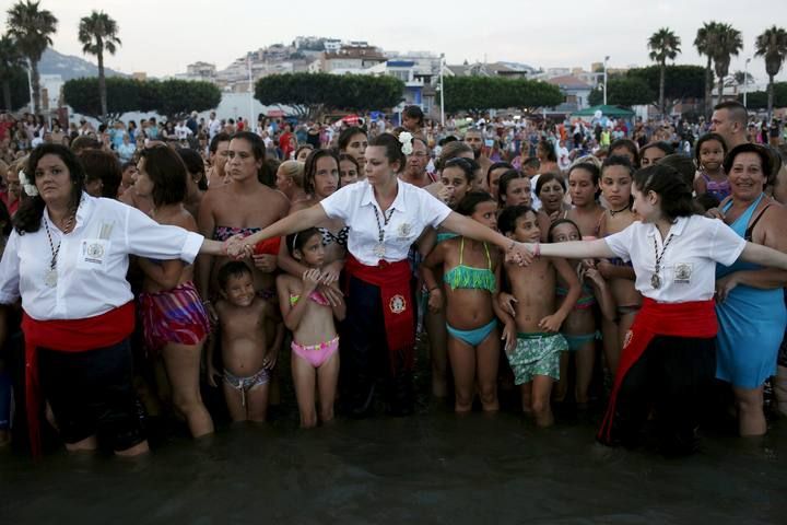 Women in traditional costumes hold hands as spectators watch the procession of the El Carmen Virgin being carried into the sea during a procession in Malaga