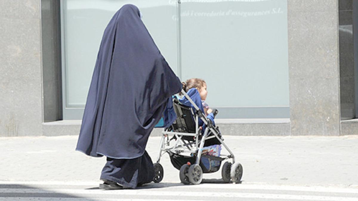 Una mujer con burka y su hijo pequeño en un cochecito.