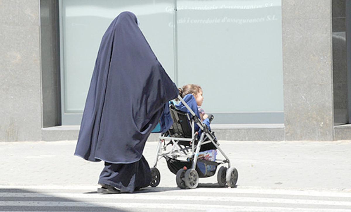 Una mujer con burka y su hijo pequeño en un cochecito.