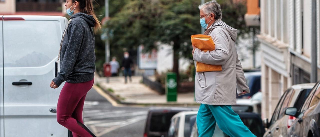 Dos mujeres cruzan un paso de peatones, una con mascarilla y otra sin ella.